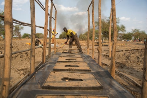 Deng Chol helps build latrines at a camp. Basic facilities such as latrines help minimize the spread of disease.