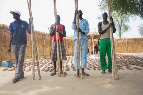 Community volunteers prepare to hand out bamboo poles, part of a CRS emergency shelter kit that includes two plastic sheets, nails, rope and metal pegs.