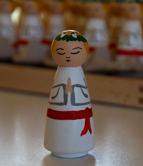 A Scandinavian-inspired St. Lucy with a wreath of candles on her head and red sash around her waist.