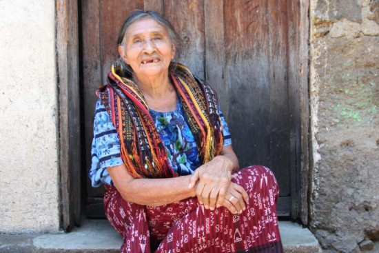 An old woman in Guatemala smiles outside her home.