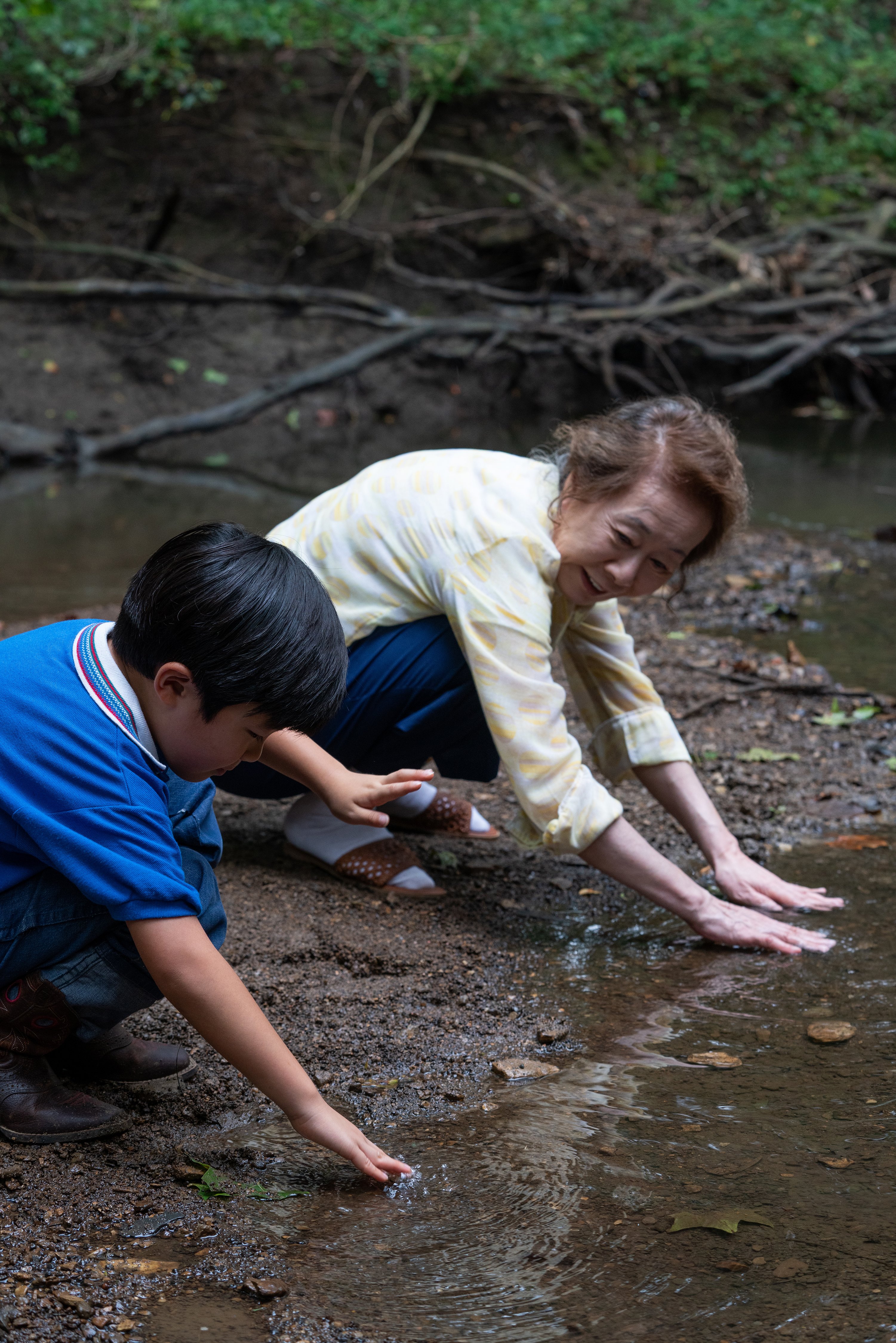 MINARI - Asian child and grandmother planting seeds by a creek