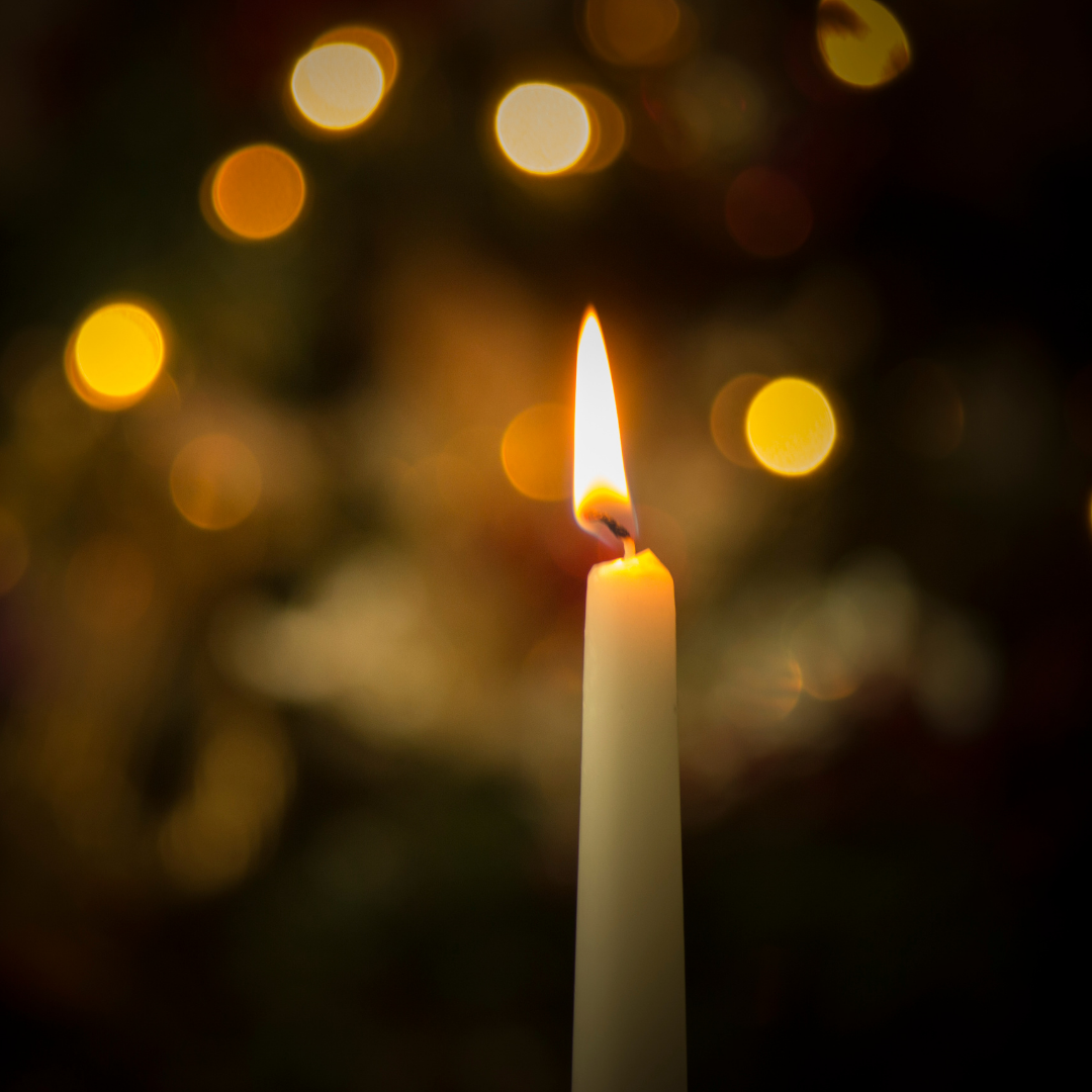 single white candle with blurred lights in background