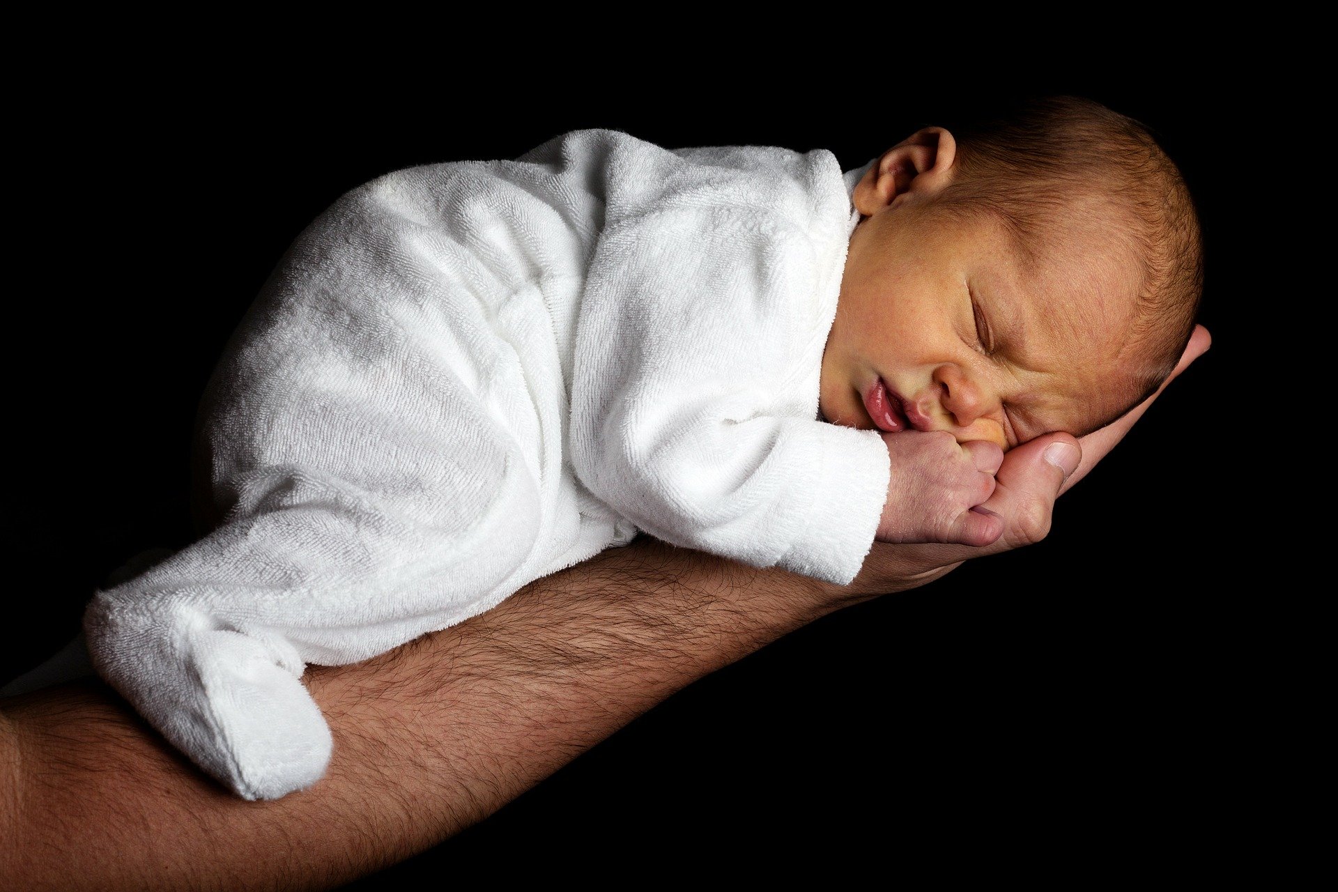 baby in white romper being held in man's arms