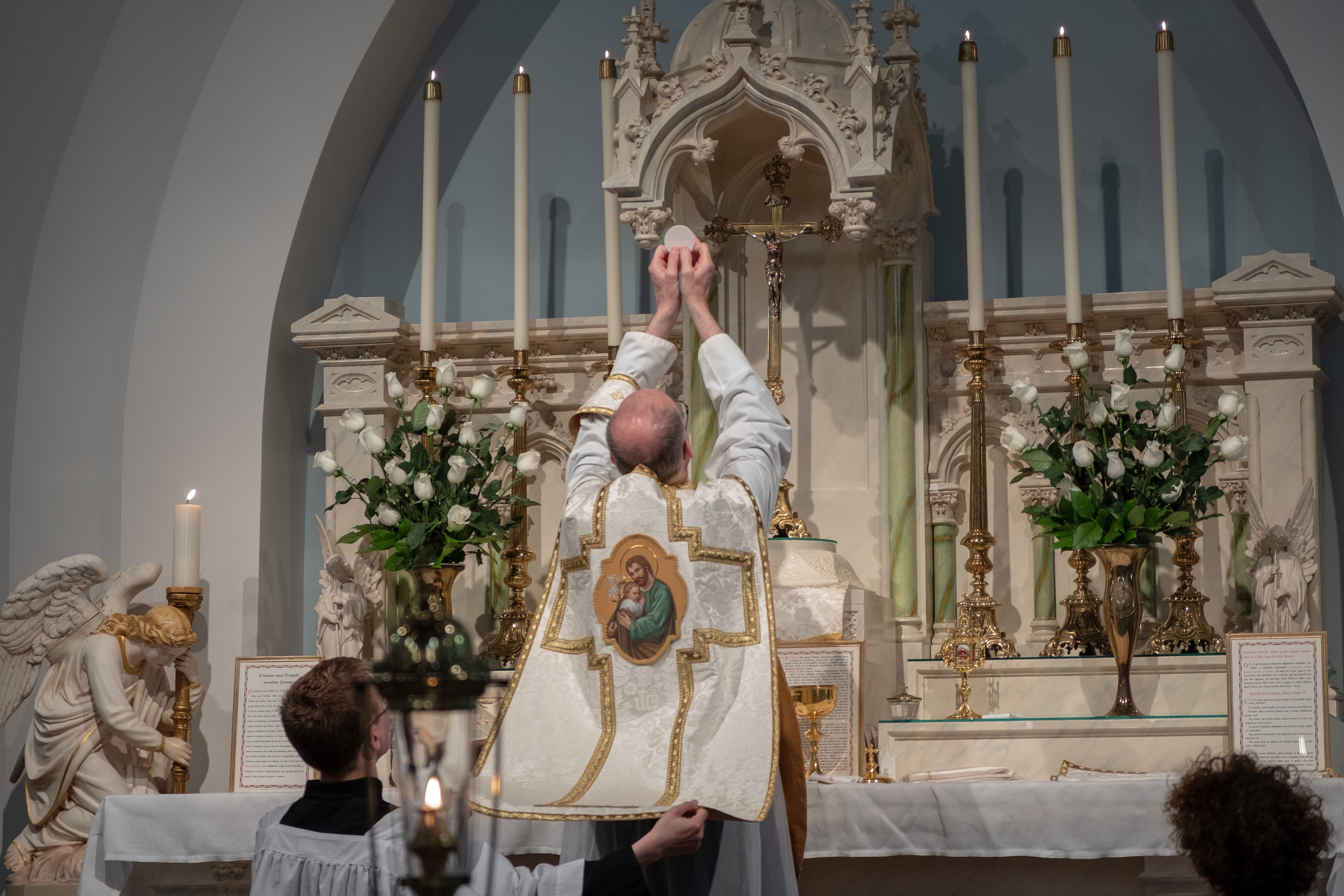Priest celebrating Mass in Extraordinary Form with altar server holding chasuble behind him